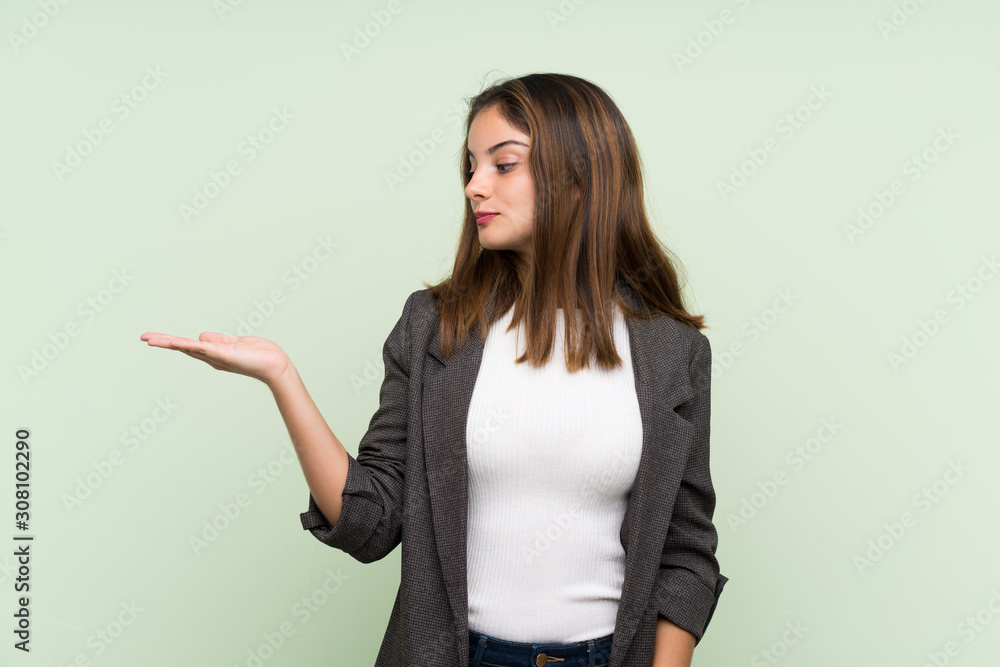 Young brunette girl with blazer over isolated green background holding copyspace with doubts Young brunette girl with blazer over isolated green background holding copyspace with doubts
