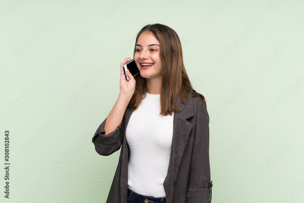 Young brunette girl with blazer over isolated green background keeping a conversation with the mobile phone Young brunette girl with blazer over isolated green background keeping a conversation with the mobile phone
