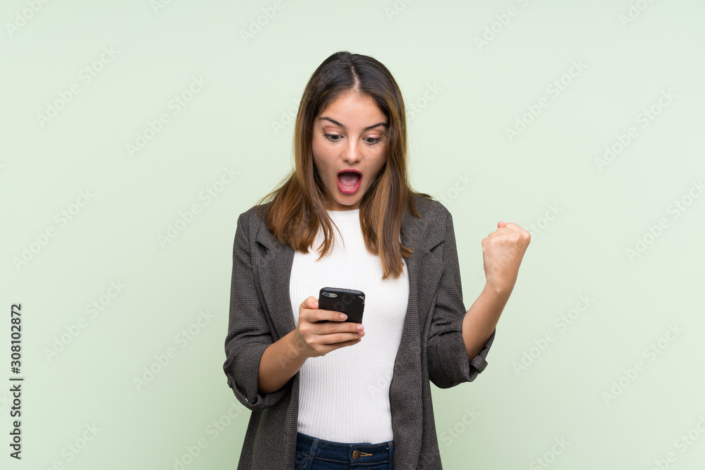 Young brunette girl with blazer over isolated green background surprised and sending a message Young brunette girl with blazer over isolated green background surprised and sending a message