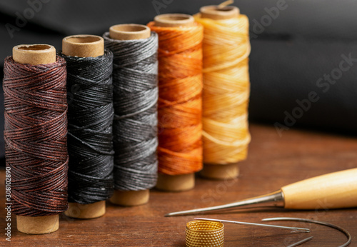 Waxed colorful sewing threads, stitching awl and needles closeup