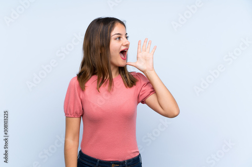 Young brunette girl over isolated blue background shouting with mouth wide open