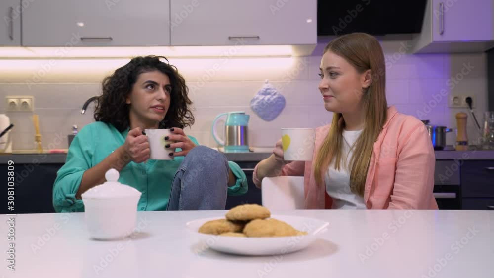 Two female friends talking while drinking tea, sitting at table, communication Two female friends talking while drinking tea, sitting at table, communication