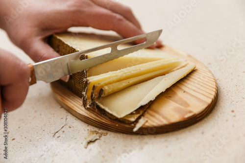 Konstfotografi manos cortando queso de oveja curado en tabla con cuchillo quesero