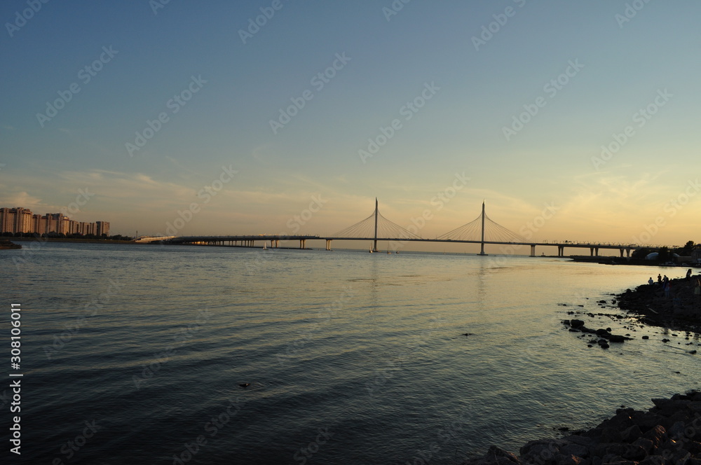 Beautiful view of the evening landscape. Water, sky, in the distance a bridge and residential buildings in the evening light of the setting sun.