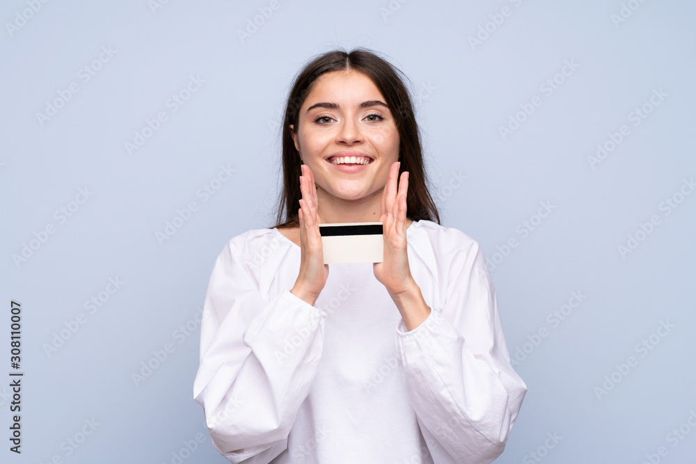 Young woman over isolated blue background holding a credit card Young woman over isolated blue background holding a credit card