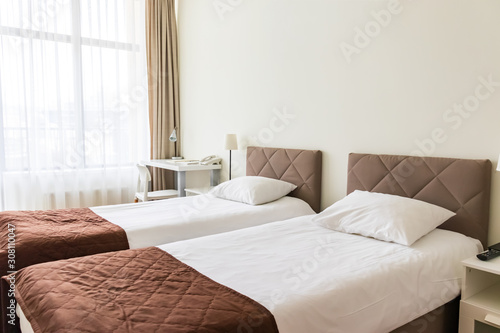 European light bedroom interior with brown, beige cozy bed and white linen, and a white nightstand near it, copy space