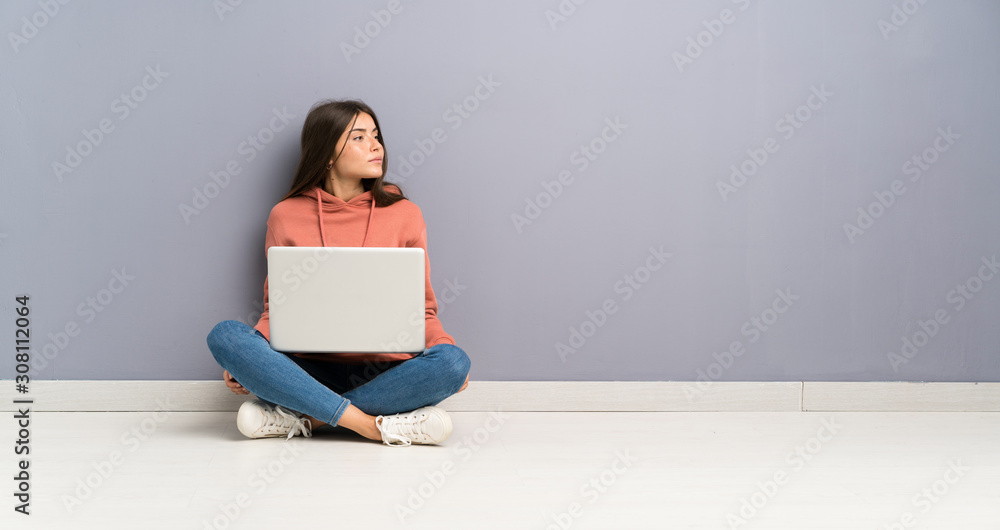 Young student girl with a laptop on the floor looking side Young student girl with a laptop on the floor looking side