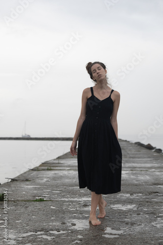 A beautiful and sad girl stands on a stone pier with a landscape on the sea. it rains