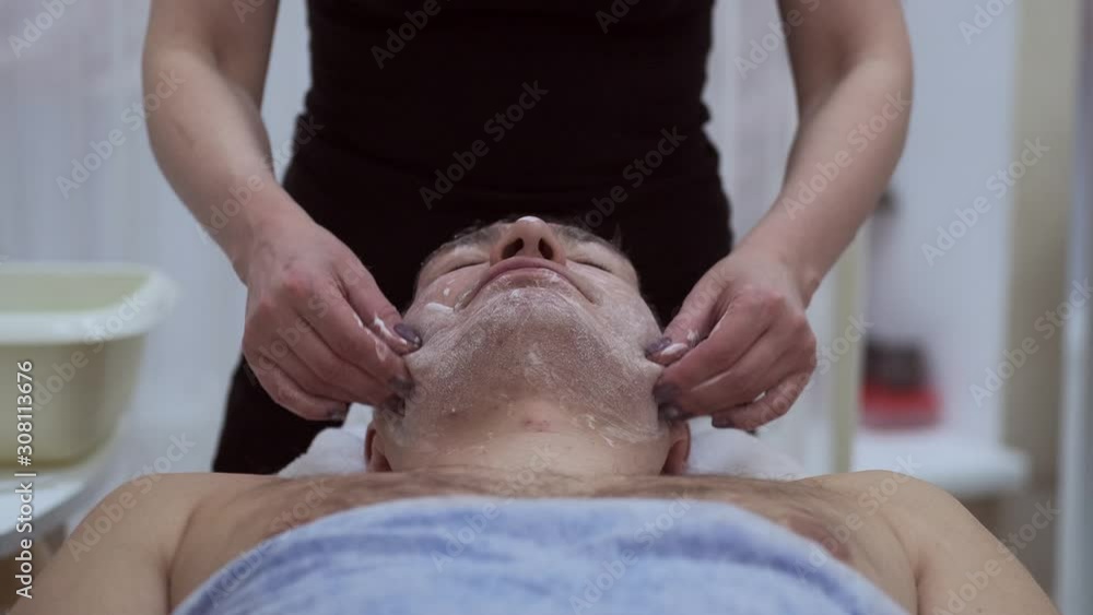 Adult man is having cosmetic treatment at spa salon. Cosmetologist medical gloves is touching face. facial cleansing with professional cosmetic facial massage. Applying the mask to the face. anti-age Adult man is having cosmetic treatment at spa salon. Cosmetologist medical gloves is touching face. facial cleansing with professional cosmetic facial massage. Applying the mask to the face. anti-age