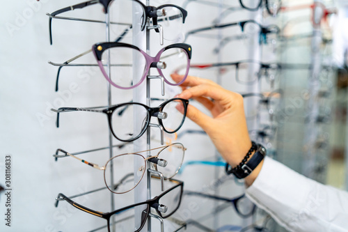 Row of glasses at an opticians. Eyeglasses shop. Stand with glasses in the store of optics. Woman's hand choosing glasses. Presenting spectacles. © Vadim