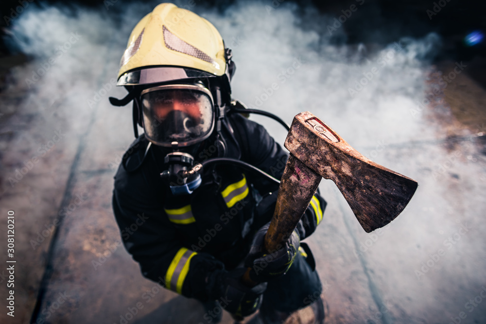Naklejka premium Portrait of a female firefighter while holding an axe and wearing an oxygen mask indoors surrounded by smoke.