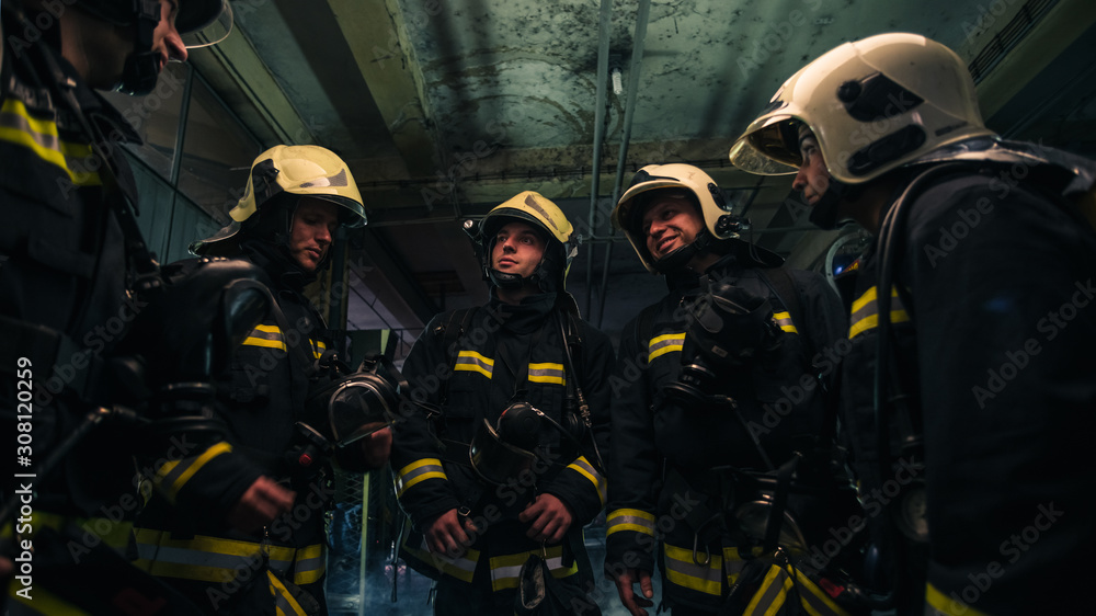 Team of firefighters standing inside ( indoors ) a buliding next to a fire engine. Team of firefighters standing inside ( indoors ) a buliding next to a fire engine.
