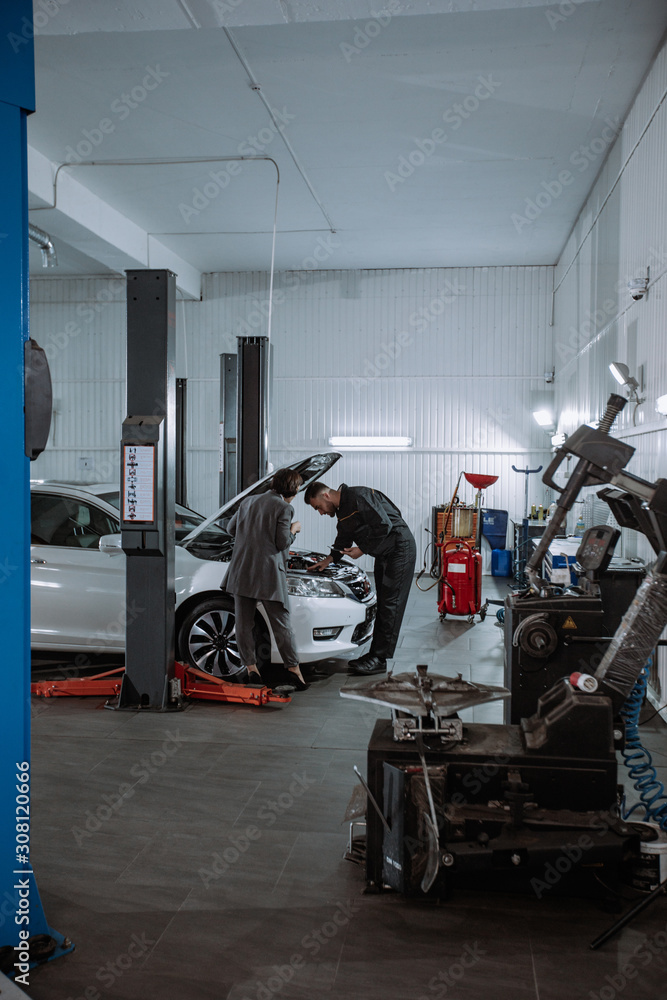 In a car service center good looking woman in a business suit her going to the car to check the problem in a auto garage In a car service center good looking woman in a business suit her going to the car to check the problem in a auto garage