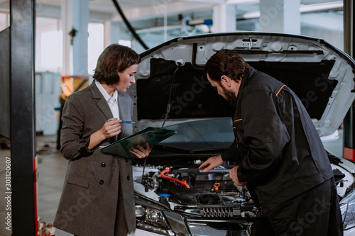 Beautiful a woman in a suit and in service auto have a conversation with the mechanic over the car he shows the problem of the car © VisionPro