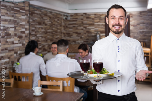 friendly waiter taking care of adults at cafe table