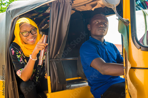 african man driving a auto rickshaw taxi being annoyed by a female passenger who's talking to him photo