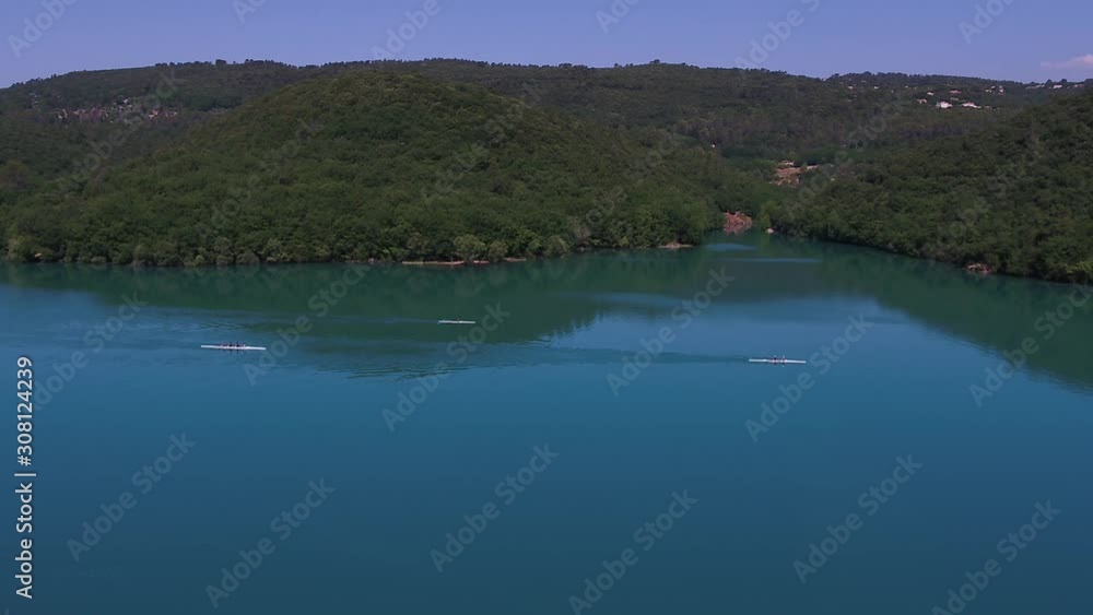Descending aerial view towards group of rowing athletes cruising woodland lake waters. Tilt up to skyline at end. Descending aerial view towards group of rowing athletes cruising woodland lake waters. Tilt up to skyline at end.