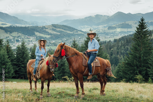 cowboy couple on horsebacks in mountains.