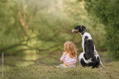 girl with long hair and borzoi dog sitting outdoors together, rear view