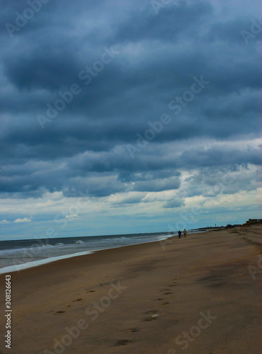 Couple walking along the ocean shore against a dramatic sky