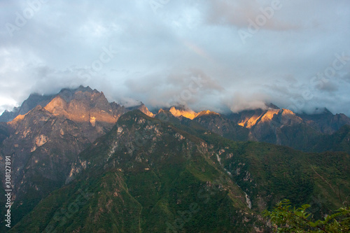 View from a guesthouse in the mountains of Yunnan during sunset with the top of the mountains being bathed in sunlight and the forests lying in the dark