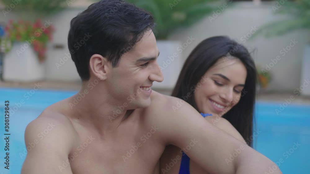 Handsome man turns and smiles to young attractive girlfriend by swimming pool Handsome man turns and smiles to young attractive girlfriend by swimming pool