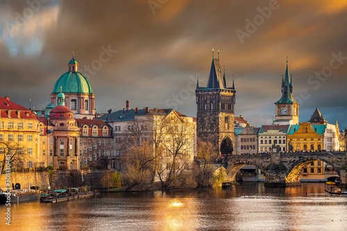 Prague  Czech Republic - The world famous Charles Bridge  Karluv most  with St. Francis of Assisi Church and clocktower with beautiful golden sunset lights and moving orange clouds on winter afternoon