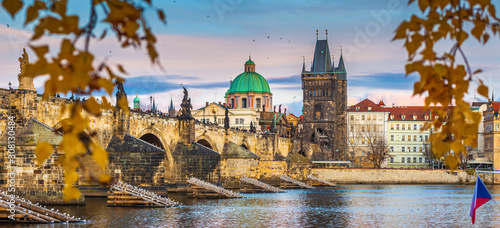 Prague, Czech Republic - Panoramic view of famous Charles Bridge (Karluv most) and St. Francis of Assisi Church dome on an autumn afternoon with Czech flag, warm sunset lights and autumn foliage