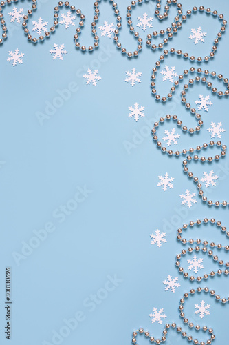 Christmas border with silver garland and stars, white snowflakes on pastel blue background. Space for text. Winter concept.