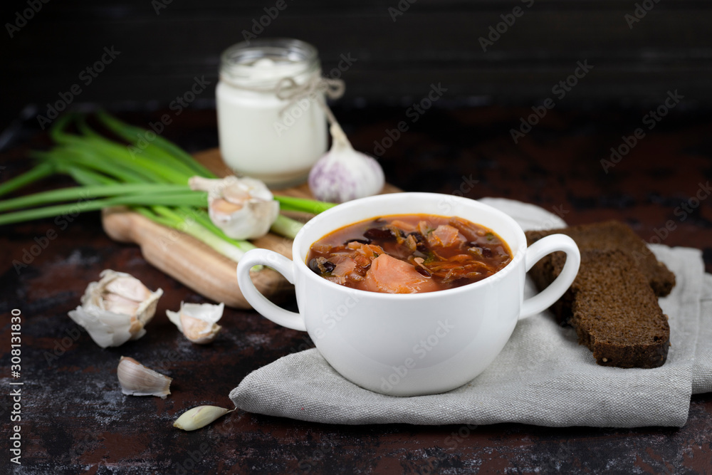  borsch, a national dish of Ukrainian cuisine. for cooking use vegetables. on the stock photo is served in a white plate with  green onions and garlic on a dark background and gray textile