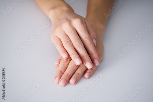 Female hands with a nice manicure on gray background, nude.