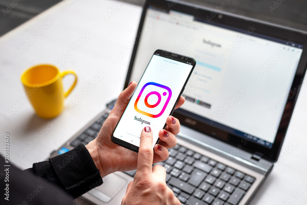 Sarajevo, Bosnia and Herzegovina - December 7, 2019: Girl uses the Instagram social network on mobile phone and laptop computer close-up