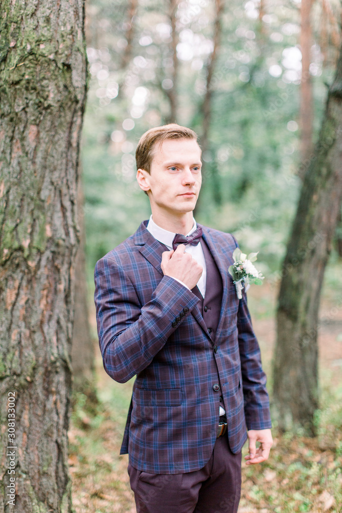 Handsome elegant groom in checkered dark violet suit is standing in the forest. Stylish wedding grooms photo. Rustic portrait. Handsome elegant groom in checkered dark violet suit is standing in the forest. Stylish wedding grooms photo. Rustic portrait.