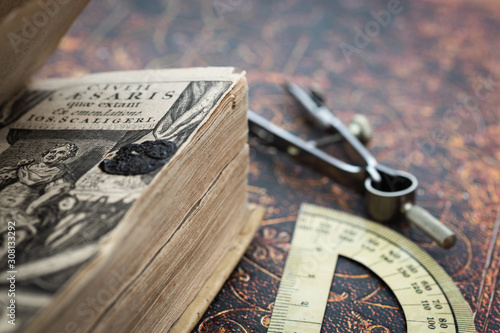 Close up photo of the front page of an authentic 17th century book from 1650. Calipers and protractor beside on an other old books cover as background. Close up, vintage latin text
