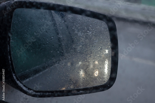 Droplets and car lights reflections through foggy car window and rear view mirror