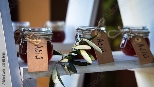 Small glass jars filled with honey, decorated with eucalyptus and a writing attached to them saying 