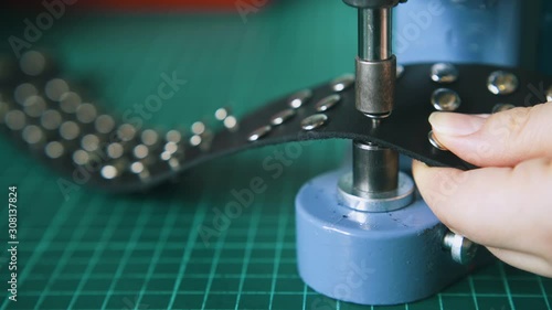 CU: Skilled worker fixes silver holnitens on stylish black leather choker on green mat in tailor workshop closeup photo