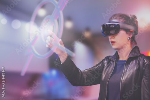 Portrait of young Caucasian woman using augmented and virtual reality with holographic hololens glasses. Pink, magenta, blue blurred background. Future technology concept. 