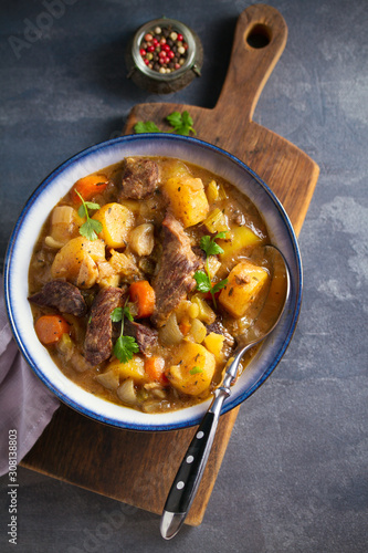 Beef meat stewed with potatoes, carrots and spices in bowl on dark gray background. Overhead vertical image