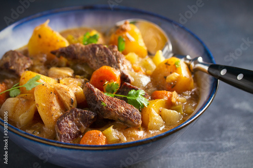Beef meat stewed with potatoes, carrots and spices in bowl on dark gray background. horizontal image