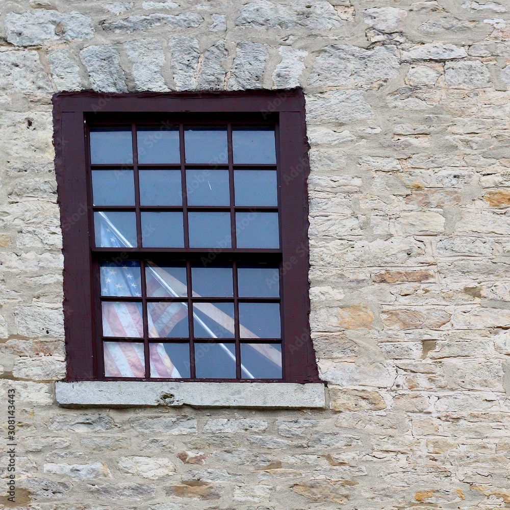 Fototapeta premium A single window on a brick building with the American Flag leaning in the window
