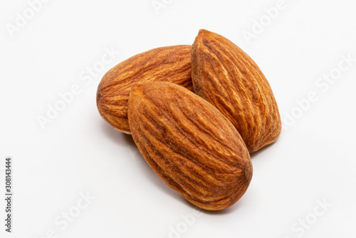 Close up shot of three roasted almonds on a white background.