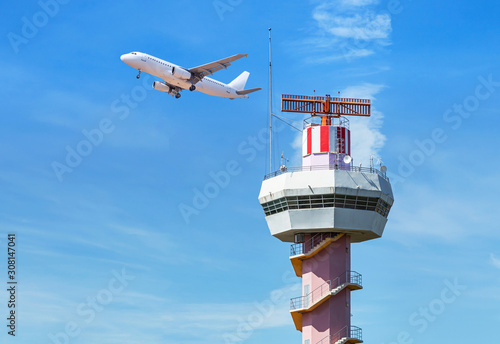 Radar  air traffic control tower in international airport while airplane taking off under blue sky.        