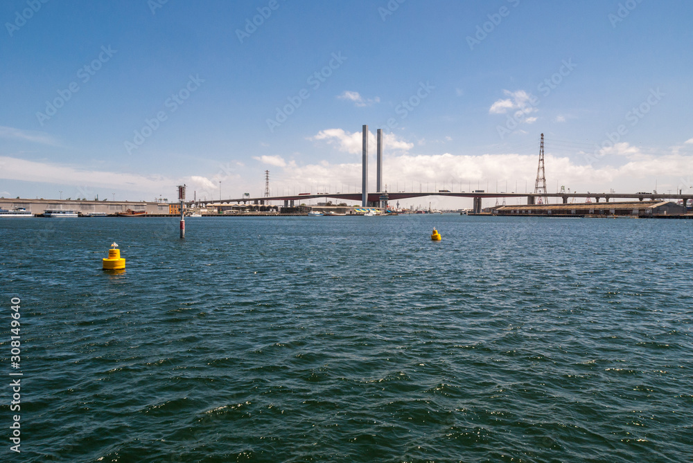 Melbourne, Australia - November 16, 2009: Wide shot of Tall and large Bolte Bridge over Yarra River under blue cloudscape. High voltage line and tower. Yellow buoys on blue water.