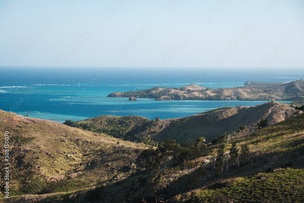 Aerial view on the green mountain tops and small village with ocean in background on Yasawa island group in Fiji, South Pacific Aerial view on the green mountain tops and small village with ocean in background on Yasawa island group in Fiji, South Pacific