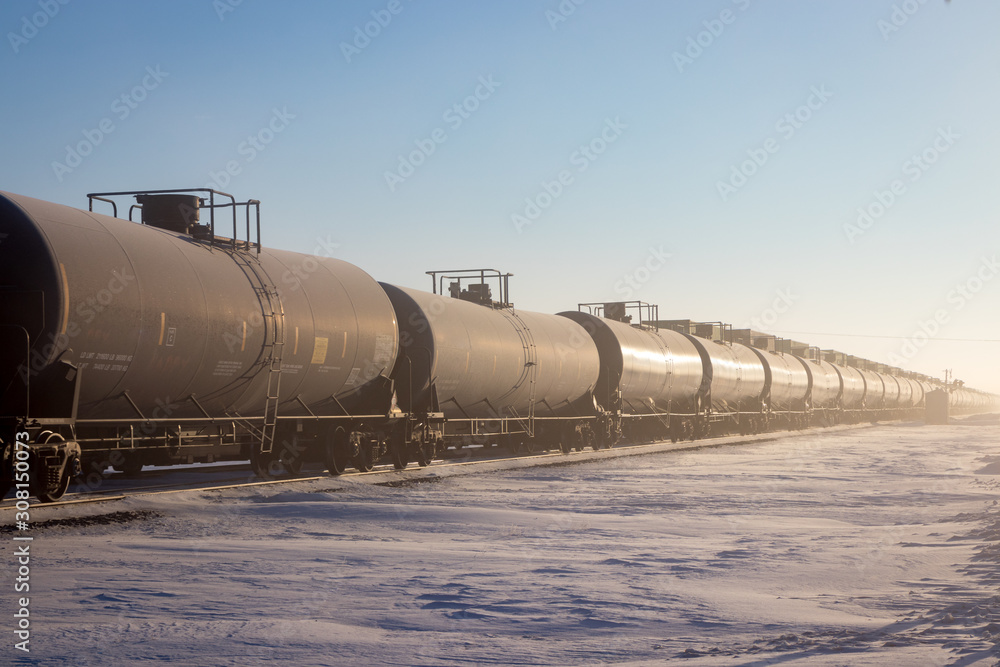Naklejka premium Line of Black Railroad Tank Cars in Winter With Snow and Blue Sky