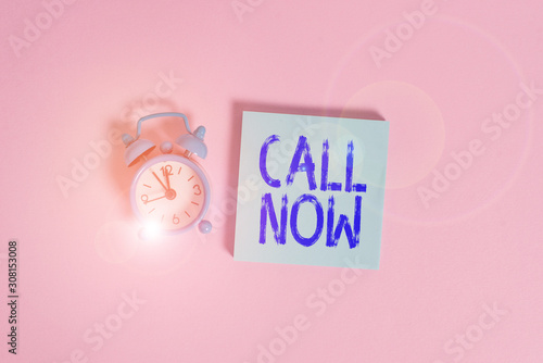 Writing note showing Call Now. Business concept for To immediately contact a demonstrating using telecom devices with accuracy Vintage alarm clock wakeup blank notepad sticky note colored background photo