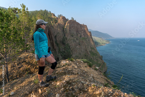 A girl stands on the edge of a high cliff and admires Lake Baikal