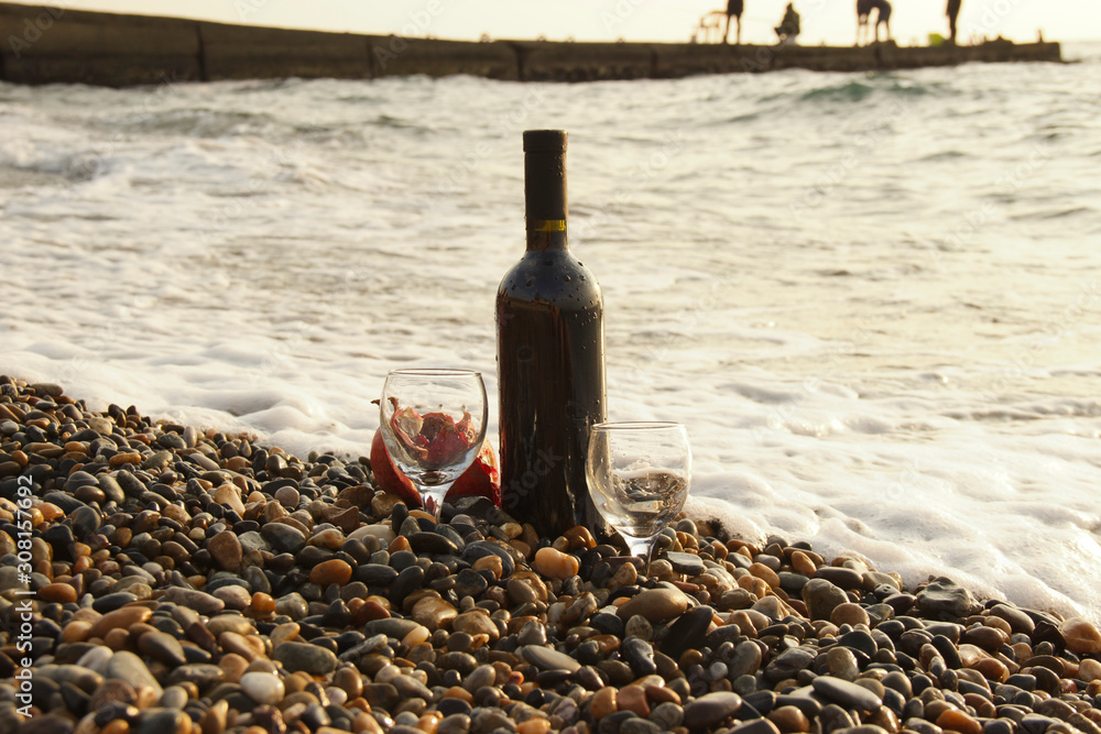 Ripe pomegranate fruit with a glass of wine and a bottle on the beach. Romantic day at the seaside. Ripe pomegranate fruit with a glass of wine and a bottle on the beach. Romantic day at the seaside.