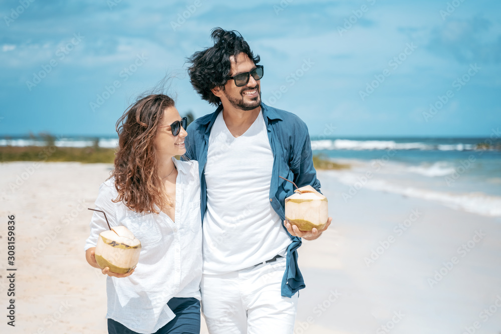 Beautiful young couple joyfully on a tropical beach with coconuts in their hands on the seashore. Honeymoon Travel and Vacation on the Tropical Ocean Beautiful young couple joyfully on a tropical beach with coconuts in their hands on the seashore. Honeymoon Travel and Vacation on the Tropical Ocean